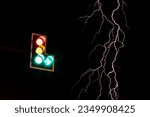Small photo of Close-up view of a traffic lamppost above an intersection road with streaks of lightning flashing from the sky during a ghastly dark pre-rain night.