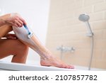 Caucasian woman shaving legs with razor blade in bathroom while sitting at the edge of the bathtub. Woman at bathroom.