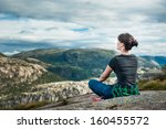 Young woman is sitting on cliff's edge and looking to a sky with clouds