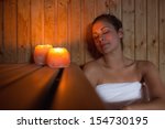 Happy brunette woman sitting in a sauna relaxing by candlelight 