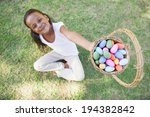Little girl sitting on grass showing basket of easter eggs to camera on a sunny day