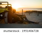 Happy caucasian couple leaning against beach buggy by the sea watching sunset. beach break on summer holiday road trip.