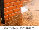 Small photo of Pressure washer using water to clean a dirty brick wall on a house.