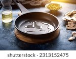 Dark frying pan with poured oil on a dark blue abstract background. Nearby is a plate of champignons, green peas, and a bottle of oil. Template for design.