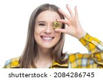 Close up portrait of a young amused smiling female holding bitcoins in front of her eyes. Concept of a bright future, wealth, innovation, investment