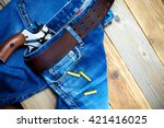 fashion old blue jeans with a leather belt and vintage revolver with cartridges. on a wooden textured background