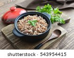 Buckwheat porridge in black casserole on wooden background closeup