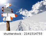 Blank directional trail signs in a beautiful winter mountain landscape with powder snow and footprints against a clear blue sky and sunbeams. Italian Alps, Italy, Europe.