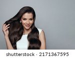 Attractive stylish happy brunette woman with long wavy hair touсhing her hair on white. Hair care and beauty concept. 