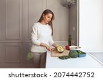Woman cooking vegetarian salad with fresh vegetables. Model cutting with knife avocados, broccoli, cale salad, cucumbers, tomatoes in white kitchen