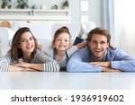 Small photo of Young Caucasian family with small daughter pose relax on floor in living room, smiling little girl kid hug embrace parents, show love and gratitude, rest at home together