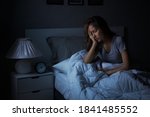 Small photo of Depressed young Asian woman sitting in bed cannot sleep from insomnia