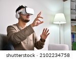 Small photo of Feeling excited and amazed. Young Asian man wearing VR goggles while playing video games with hands reaching out to touch something in virtual world.