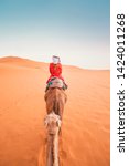 Small photo of A tourist girl with a traditional moroccan red dress riding a dromedary in the Sahara desert of Merzouga, Morocco