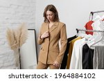 Young woman choosing clothes and trying on beige blazer in fashion atelier or personal wardrobe.