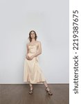 Small photo of Female model wearing beige camisole silk top and wrapped midi skirt. Stylish and elegant monochrome summer outfit. Fashion Studio shot.