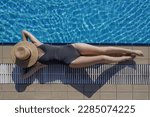 Top view of young woman enjoying day at the pool, laying down at the edge covering face with straw boater hat. Summer vacation concept.	