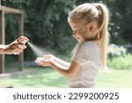 Mother applying hand sanitizer or mosquito repellent spray on her child's hand