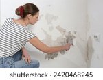 Small photo of Saltpeter on the wall problem. Woman is using a scraper to scrape and remove all loose paint and plaster that is in poor condition, until a firm surface is achieved.