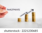 hand holding Investment text in front of growing stacks of coins with arrow pointing upward, metaphor of increasing your savings and compound interests