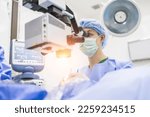 Small photo of Male doctor doing surgery inside modern operating theater in surgical hospital.Microscope was use in eye surgery.Surgeon in blue sterile suit working with microscope with light effect.Medical concept.