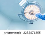 Small photo of Doctor or surgeon in blue gown holding surgical lamp to adjust light inside operating theatre with space in background.People did surgery in hospital.Nurse with medical glove in operating room.