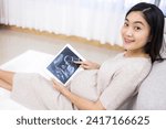 Small photo of Pregnancy pointing digital tablet. Pregnant woman holding smart tablet.Beautiful Asian pregnant points at screen after IVF treatment for infertility.Fetus well-being.Happiness feeling with smile.