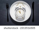 Small photo of White plate and clock on a dark background with copy space. Concept of interval fasting and autophagy.