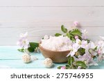 Spa or wellness setting. Sea salt in bowl and apple blossom on turquoise wooden background against white wall. Selective focus is on salt.