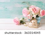 Pink roses flowers  in vase  and decorative heart on white painted wooden background against turquoise wall. Selective focus. Place for text.