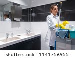 Small photo of Janitor woman or charlady with her work tools looking at camera in toilet