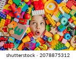 Funny surprised little girl lying in the chaos of toys. Kid