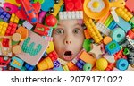Small photo of Funny shocked toddler girl among a lof her toys. Kid's face among od variety of toys. Horizontal panoramic banner. Top view, flat lay.