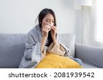 Young Sick Asian Woman Sitting under the Blanket Whiles Sneezing  with Tissue on the Sofa