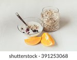 Yogurt with berries currants, a spoon, a jar with oat flakes and orange on a light table.