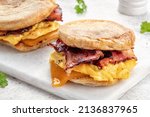 English muffin, scrumbled egg, ham, and cheese breakfast sandwich on a cutting board