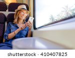 Enjoying travel. Young pretty woman traveling by the train sitting near the window using smartphone.