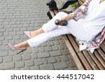 Summer outfit, street fashion look. Young tanned beautiful woman in white pants and light floral pink patent in leather high-heeled shoes. Stylish girl sitting on a bench in the city. 