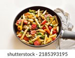Penne pasta with roasted vegetables in pan over light stone background. Close up view