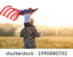 Rear view of military man father carrying happy little son with american flag on shoulders and enjoying amazing summer nature view on sunny day, happy male soldier dad reunited with son after US army