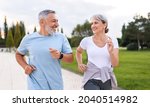 Small photo of Happy senior husband and wife in sportive outfits running outdoors in city park, lovely retirees couple jogging in sunny morning looking at each other with warmth and smile. Healthy lifestyle concept