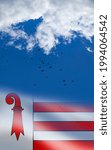 Small photo of Flag of Jura cantons of Switzerland with flying birds in blue cloudy sky. The red crosier resembles a shepherd's crook of bishops. Independence day, 23 June.