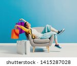 Cheerful happy shopaholic woman with lots of shopping bags, she is sitting on an armchair and celebrating with arms raised
