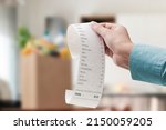 Small photo of Woman checking a grocery receipt and bag full of groceries in the background