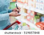 Woman doing grocery shopping at the supermarket, she is pushing a cart and checking items on a list