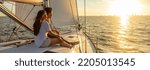 Small photo of Panorama of young Hispanic couple at leisure sailing the ocean relaxing on luxury yacht watching the sunset on the horizon