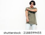 Portrait of handsome confident  stylish hipster lambersexual model.Sexy man dressed in over size T-shirt and jeans. Fashion male isolated in studio. Posing near white wall