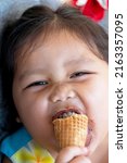 Small photo of Asia girl happily eats a chocolate cone and her mouth smacks of ice cream.