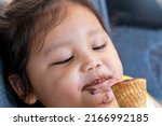 Small photo of Asia girl happily eats a chocolate cone and her mouth smacks of ice cream.