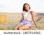 Adorable happy smiling ittle girl child sitting on a hay rolls in a wheat field at sunset